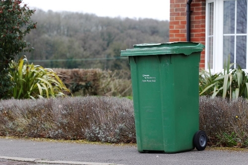 A garden waste green bin at the end of someone's driveway.