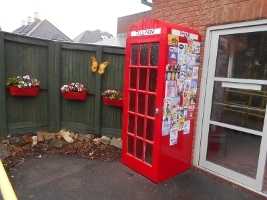 An image of a decorated, red telephone box and wall plant pots full of flowers at Hungerford Resource Centre