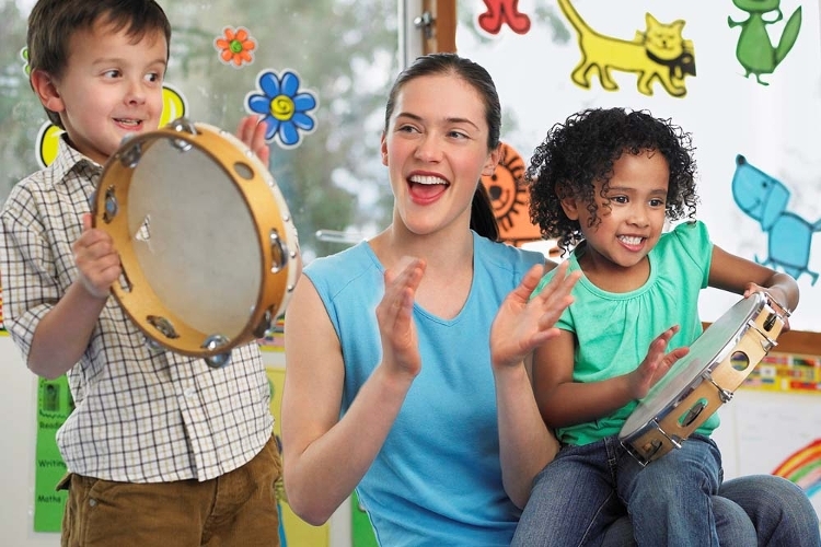 An image of a woman clapping along with two children playing on tambourines