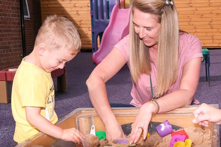 An image of a woman and a child playing in a sand pit