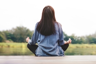 An image of a woman in the lotus yoga pose, facing away looking at a lake