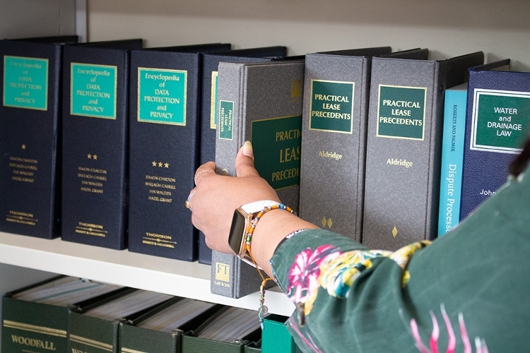 A person taking a folder of legal information off of a bookshelf.