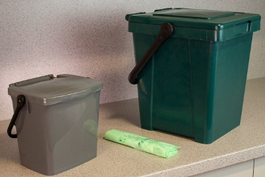 A indoor and outdoor food waste caddy on a kitchen worktop, next to a roll of compostable bags.