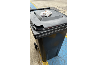 A black rubbish bin with a clear bag of batteries on top.